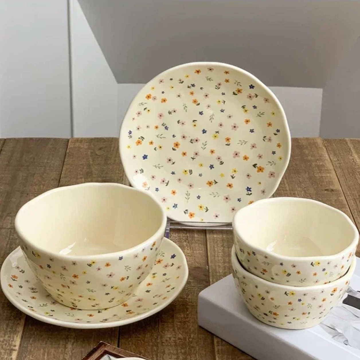 An image showing three of the Plantish Wildflower Collection - the Wildflower Plate, and the Wildflower Bowl in both the Small and Large Sizes, all on a wood table.