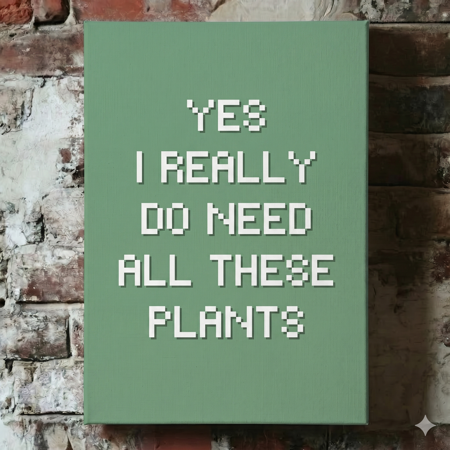 A Plantish canvas showing the phrase "Yes I Really Do Need All These Plants" in a white font against a green background, hanging on a red brick wall.