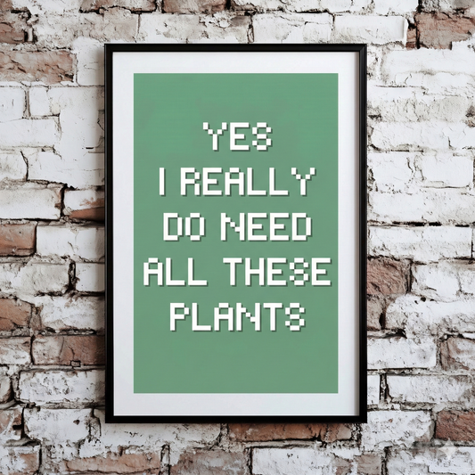 A Plantish print showing the phrase "Yes I Really Do Need All These Plants" in a white font against a green background, hanging on a brick wall.